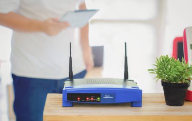 Bir kablosuz yönlendiriciye yakın çekim ve ofisteki oturma odasında akıllı telefon kullanan bir adam, evden çalışma için ekipman, Covid-19 sağlık krizi sırasında karantina izolasyonu sırasında.       