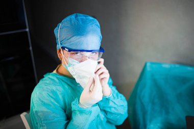 Üniformalı, gözlüklü ve maskeli kadın doktor hastanede yoğun çalışıyor. Bir cerrahın portresi