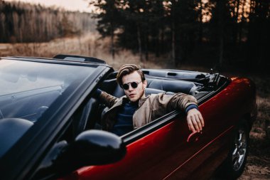 Yazın gün batımında üstü açık bir arabada güneş gözlüklü genç bir erkek sürücü. seyahat kavramı