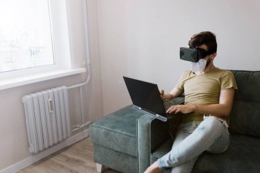 Tıbbi maskeli bir adam evde dizüstü bilgisayarla çalışıyor, kendini karantinaya alıyor..