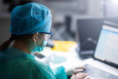 Üniformalı, gözlüklü ve maskeli kadın doktor hastanede yoğun çalışıyor. Bir cerrahın portresi