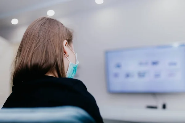 girl in a medical mask on quarantine self-isolation watches TV.