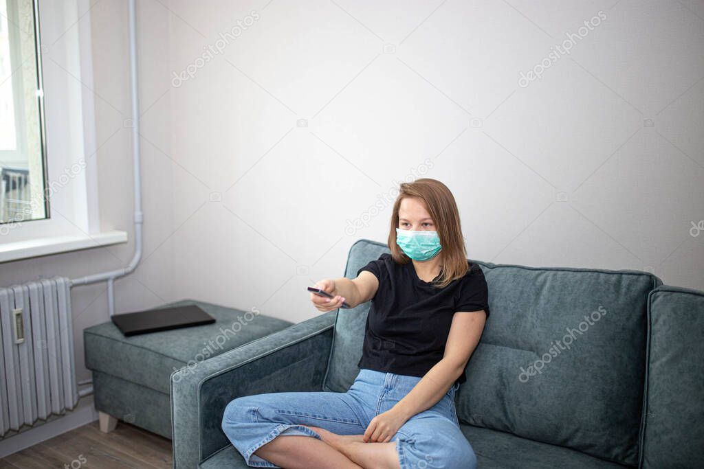 girl in a medical mask on quarantine self-isolation watches TV.