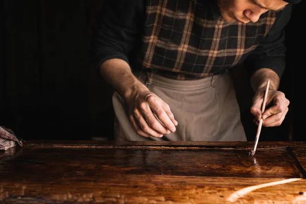 craftsman works in a workshop with wood, varnishes a wooden element of furniture.