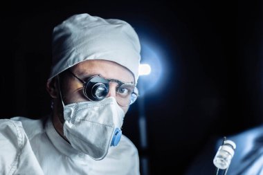 Üniformalı ve gözlüklü bilim adamı cam büyüteçle virüsün maddesini kapsülde inceliyor. laboratuvar testleri.