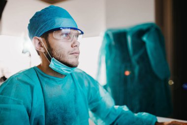 Coronavirus salgını sırasında ameliyat odasında üniformalı ve gözlüklü genç cerrah..