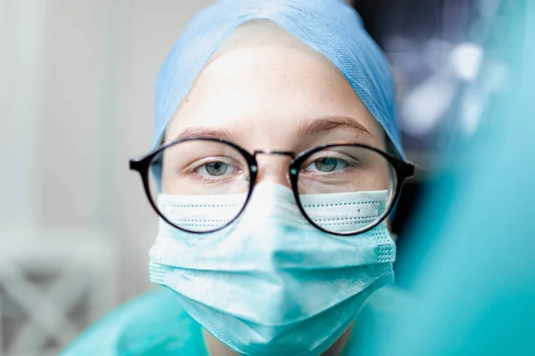 young woman surgeon doctor in uniform and goggles in operating room during pandemic.