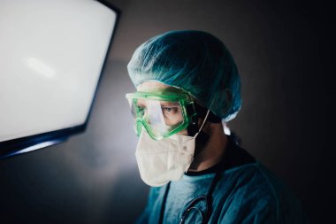 Koruyucu üniformalı bir adam ve epidemiyoloji uzmanı gözlüklü bir adam geceleri hastanede ekrana bakıyor.