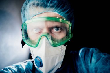 Koruyucu üniformalı bir adam ve epidemiyoloji uzmanı gözlüklü bir adam geceleri hastanede ekrana bakıyor.