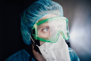 Koruyucu üniformalı bir adam ve epidemiyoloji uzmanı gözlüklü bir adam geceleri hastanede ekrana bakıyor.