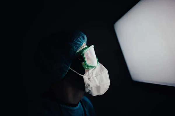 夜に病院の画面を見る疫学者の医師の防護服を着た男 — ストック写真