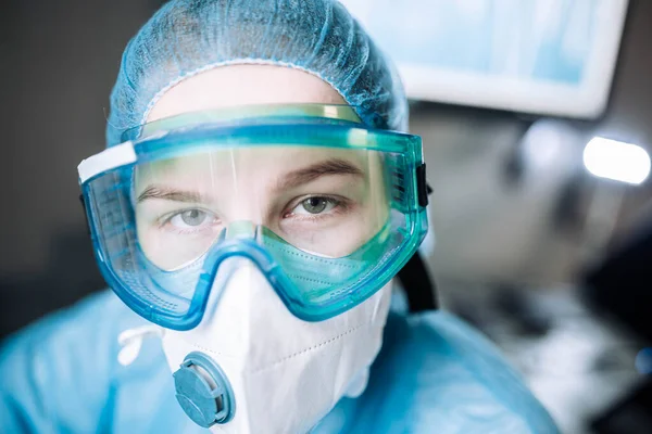 young woman surgeon doctor in uniform and goggles in the operating room during a pandemic.