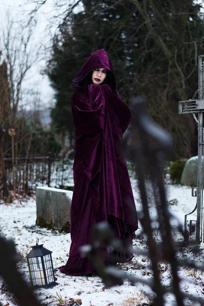 Woman Witch in a raincoat in a cemetery with crosses and skulls