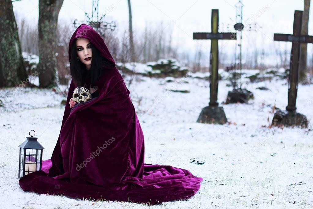 Woman Witch in a raincoat in a cemetery with crosses and skulls