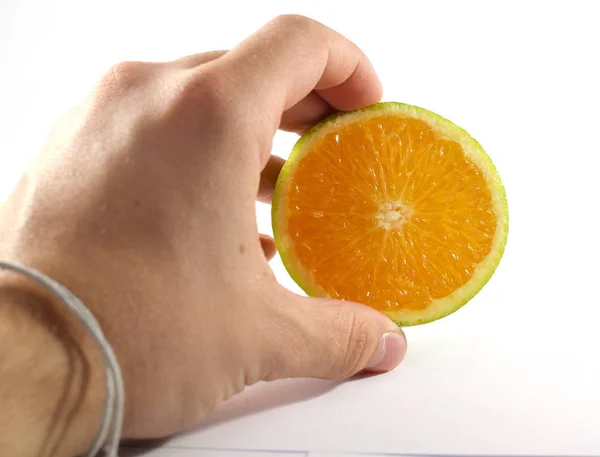 Mano masculina sosteniendo la mitad de una fruta naranja cortada — Foto de Stock
