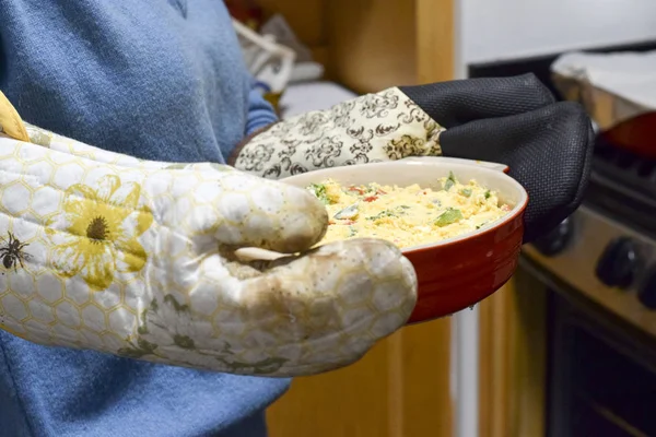 Woman with oven mitts holding