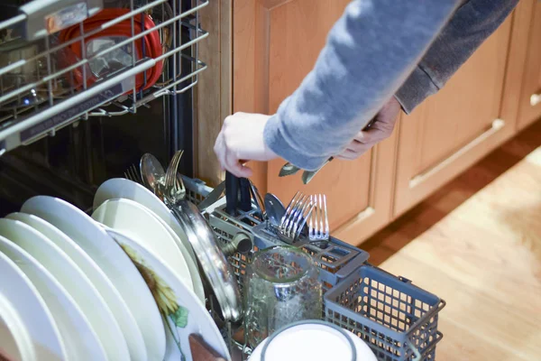 Женщина загружает посуду и столовое серебро в посудомоечную машину — стоковое фото