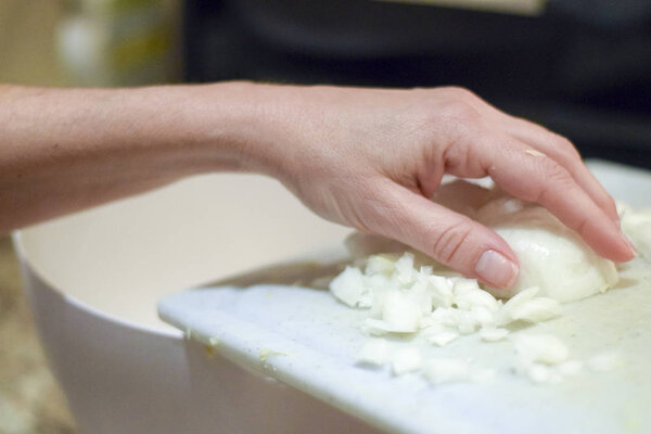 Рука соскребает нарезанный лук с доски
