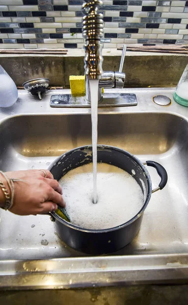 Hand washing sauce pot with a sponge in sink