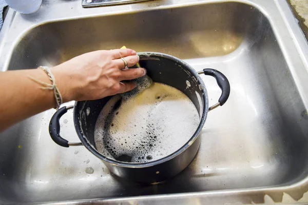 Hand washing sauce pot with a sponge in sink