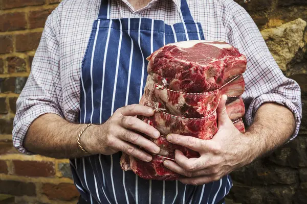 Carnicero en delantal sosteniendo trozo de carne — Foto de Stock