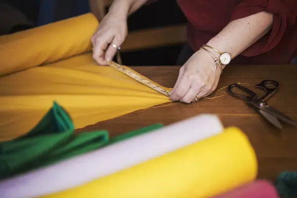 Woman using tape measure to yellow fabric — Stock Photo, Image