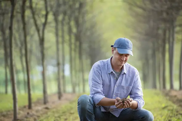 Man Cap Crouching Examining Handful Soil Park Rows Trees — Stock Photo, Image