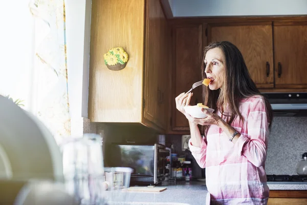 Senior woman eating in a kitchen — Stock Photo