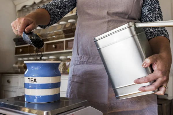 Close-up of woman standing in a kitchen, placing loose tea into striped blue ceramic jar. — Stock Photo