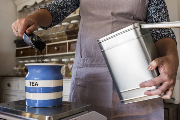 Primer plano de la mujer de pie en una cocina, la colocación de té suelto en el frasco de cerámica azul rayado . - foto de stock