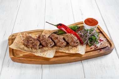 Kızarmış sebzeli ve ahşap masada kırmızı soslu koyun eti kebabı.