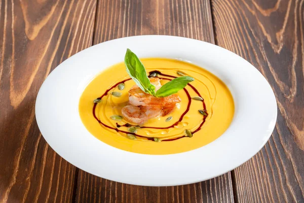 Тарелка тыквенного кремового супа с креветками и базиликом на деревянном столе — стоковое фото