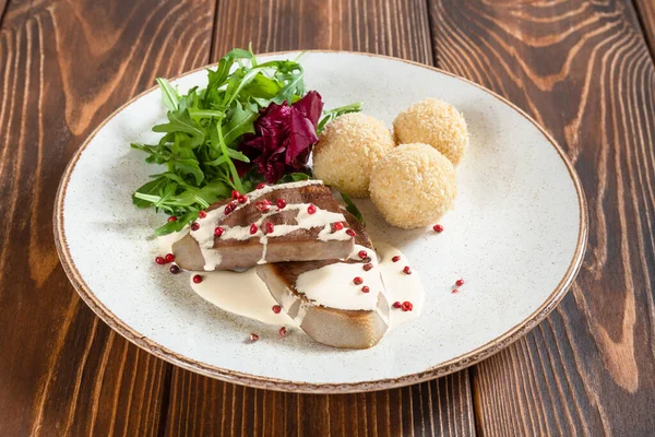 Язык говядины со сливочным соусом и сырные шарики с салатом из ракеты на деревенском деревянном столе — стоковое фото