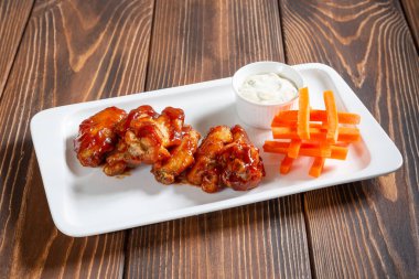 Tavuk kanatlı sıcak aperatif barbekü, havuç ve ahşap masada beyaz sos.