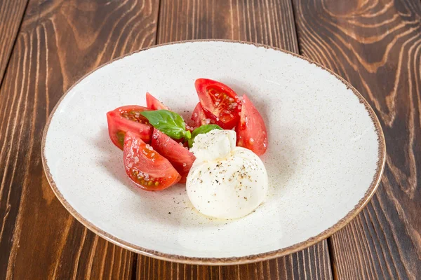 Тарелка салата капрезе - свежие помидоры и кусочек сыра моцарелла на деревянном столе — стоковое фото