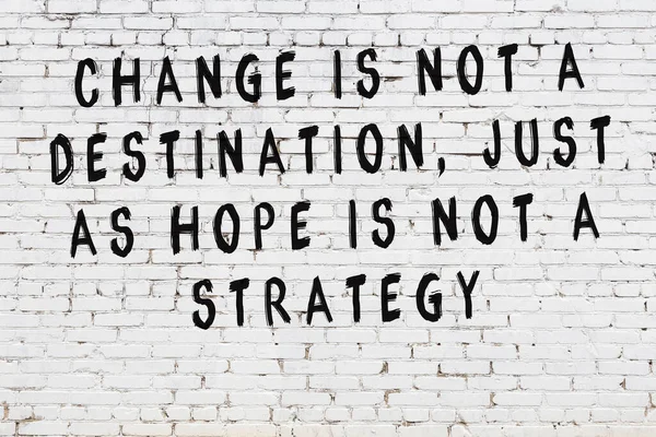 Beyaz tuğla duvara zekice alıntılar yazılı siyah bir yazı.