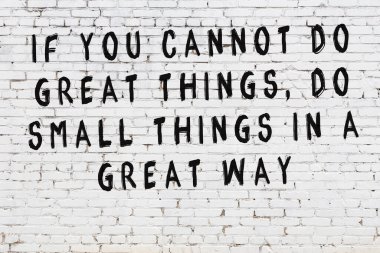 Beyaz tuğla duvara zekice alıntılar yazılı siyah bir yazı.