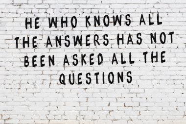 Beyaz tuğla duvara zekice alıntılar yazılı siyah bir yazı.