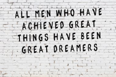 Beyaz tuğla duvara zekice alıntılar yazılı siyah bir yazı.