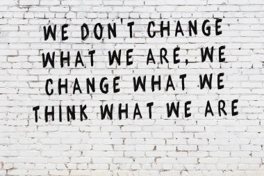 Beyaz tuğla duvara zekice alıntılar yazılı siyah bir yazı.