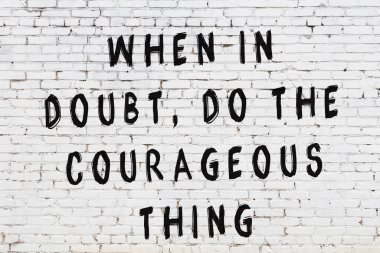 Beyaz tuğla duvara zekice alıntılar yazılı siyah bir yazı.