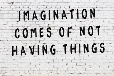 Beyaz tuğla duvara zekice alıntılar yazılı siyah bir yazı.