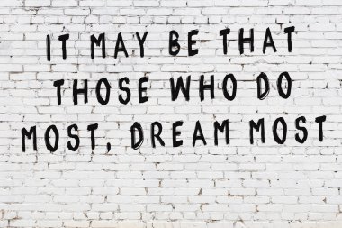 Beyaz tuğla duvara zekice alıntılar yazılı siyah bir yazı.