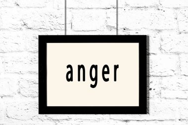 Beyaz tuğla duvarda asılı siyah çerçeve ve yazılı öfke