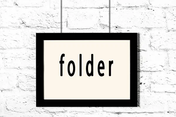 Black frame hanging on white brick wall with inscription folder — Stock Photo, Image