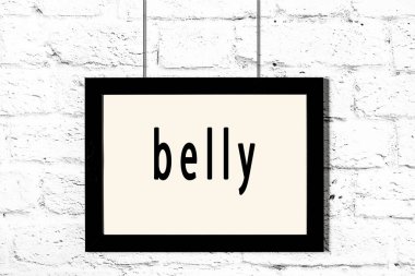 Beyaz tuğla duvarda asılı siyah çerçeve ve yazılı göbek.