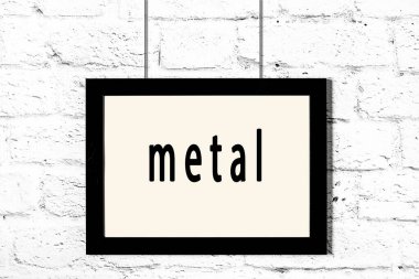 Beyaz tuğla duvarda yazılı siyah çerçeve asılı.