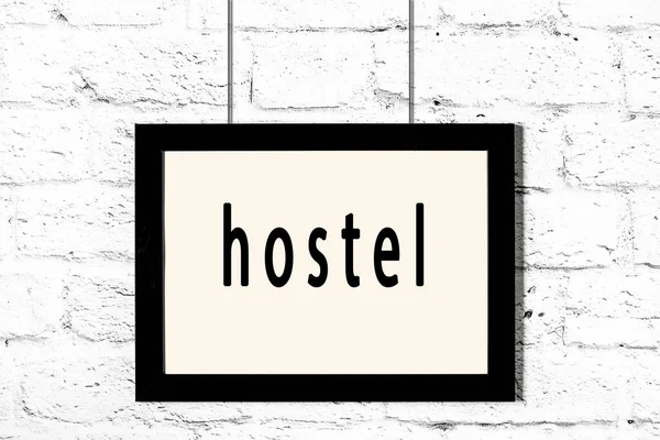 Black frame hanging on white brick wall with inscription hostel — Stock Photo, Image