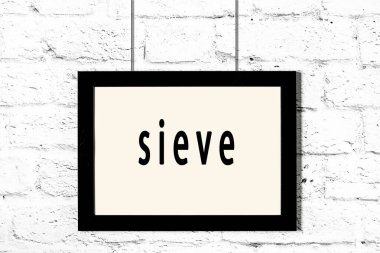 Beyaz tuğla duvarda asılı siyah çerçeve ve elek.