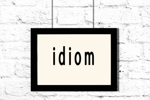 Black frame hanging on white brick wall with inscription idiom — Stock Photo, Image